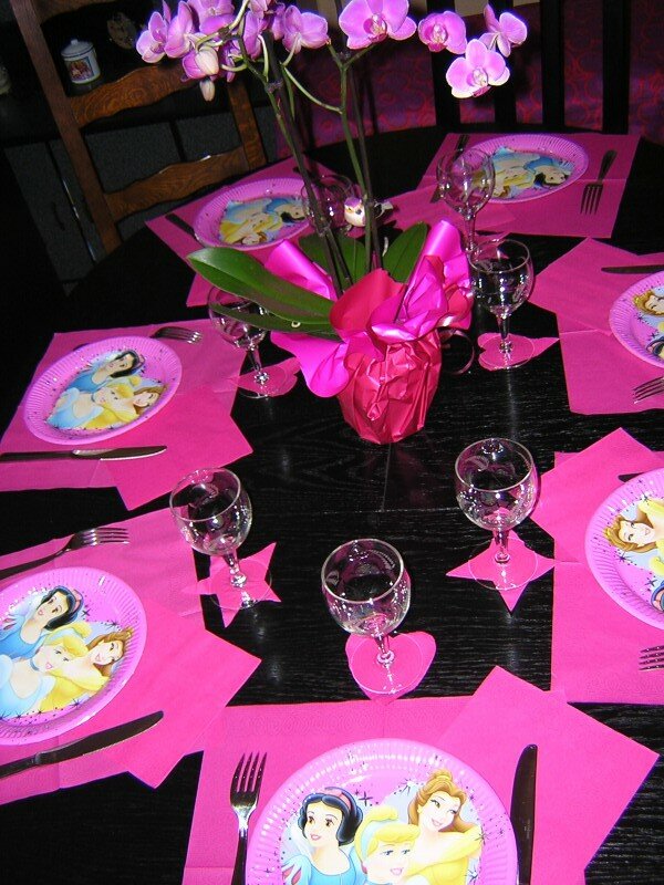 Une Fille Est Assise à Une Table Avec Une Nappe Rose Et Un Gâteau En Forme  De Coeur Rose.